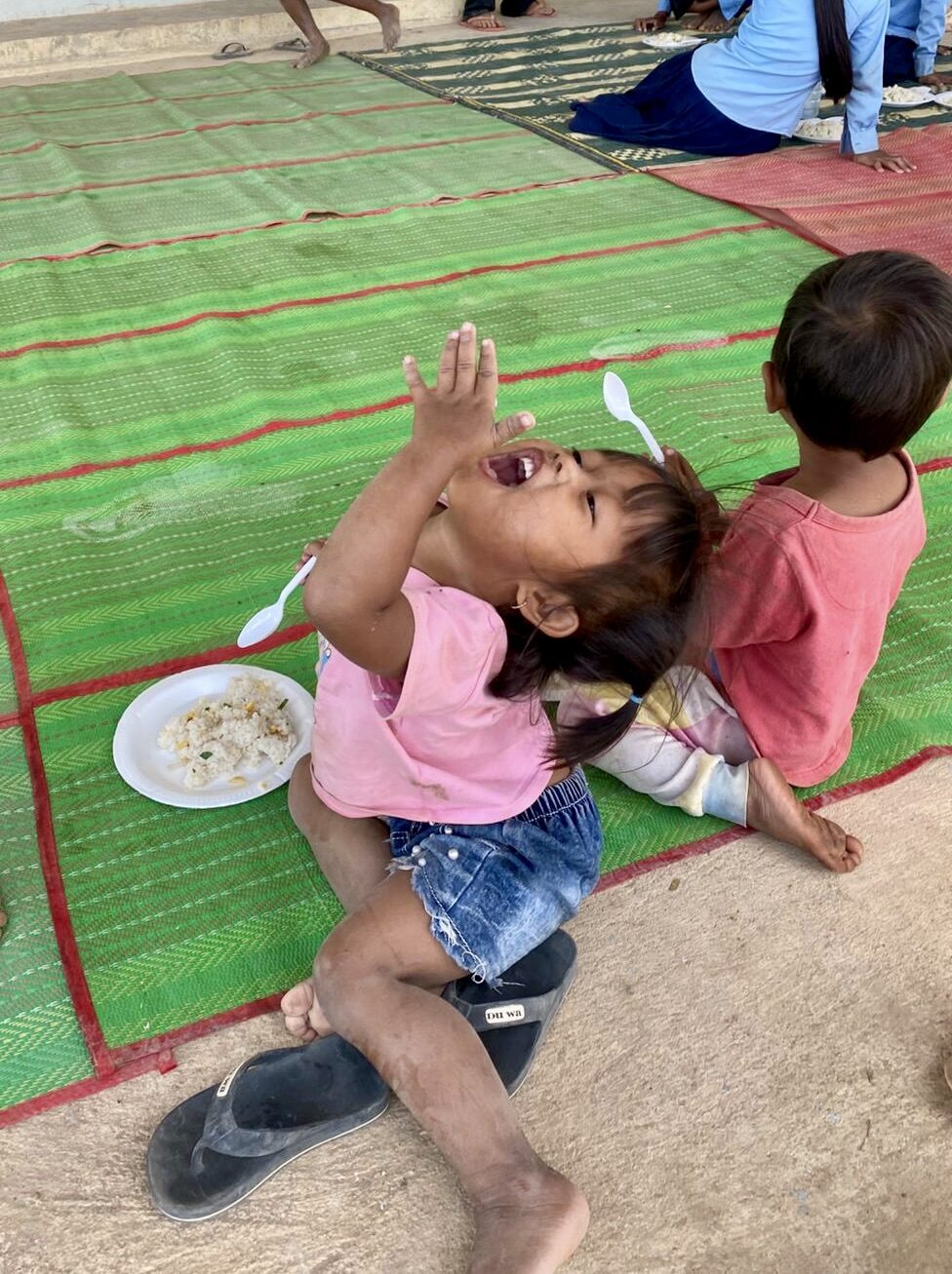 A child laughing while tossing food at a community meal in Pursat