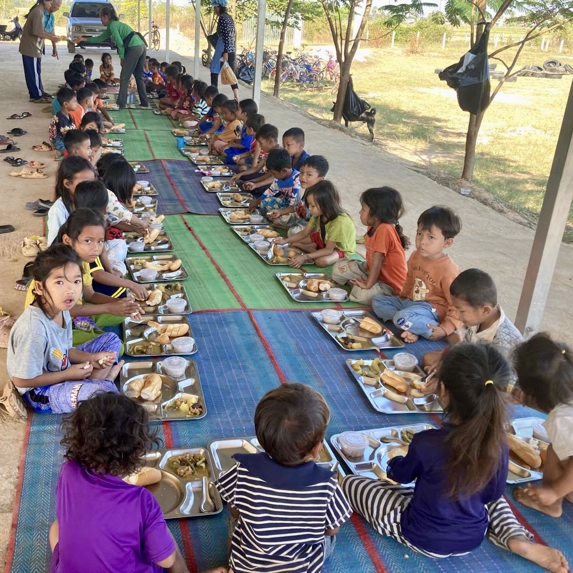 Dozens of children sharing a meal together on long woven mats