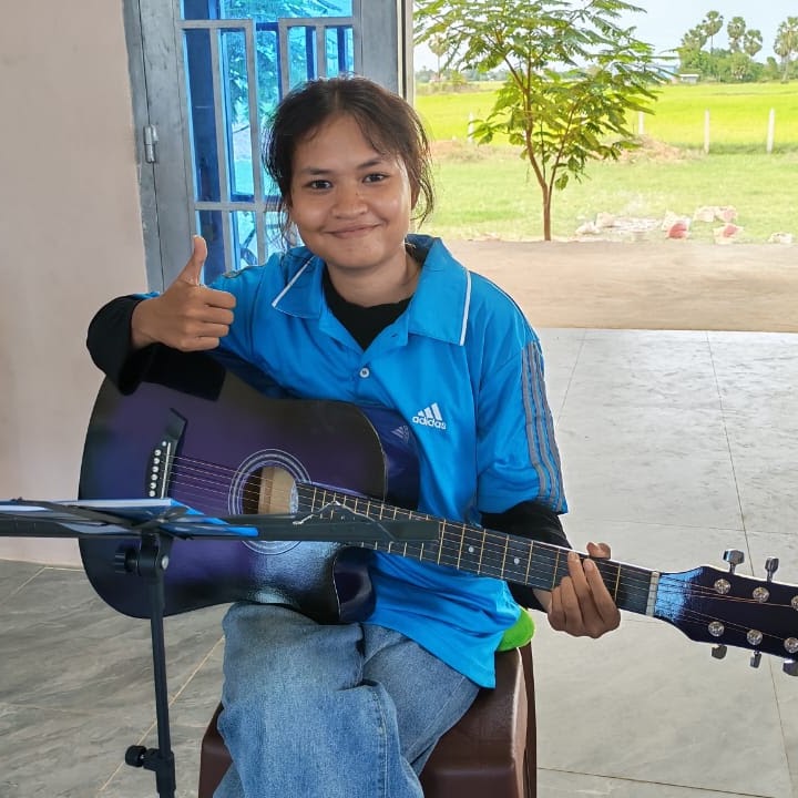 A teenage girl smiling with a guitar during youth music ministry