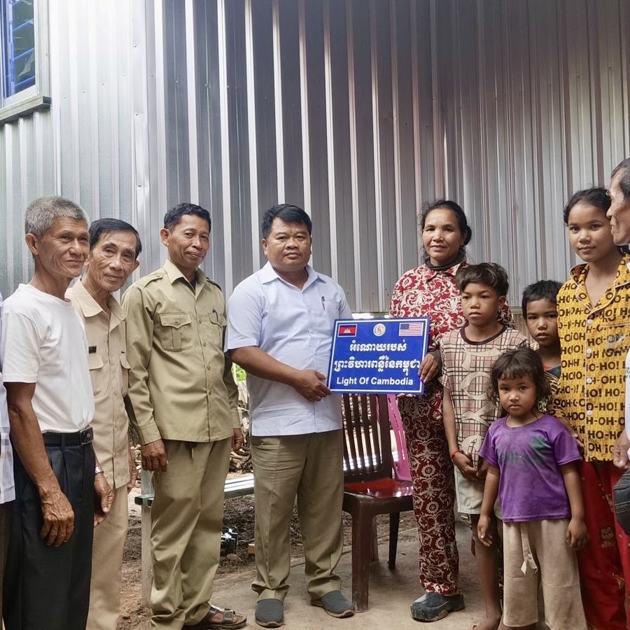 A family and local leaders in Pursat holding the Light of Cambodia sign outside their home