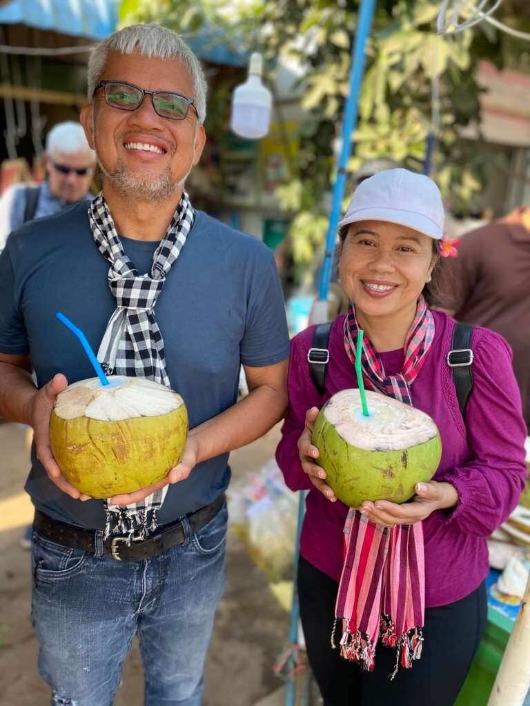 Sydney and Nareth Meth outside in Cambodia, sharing a fresh coconut
